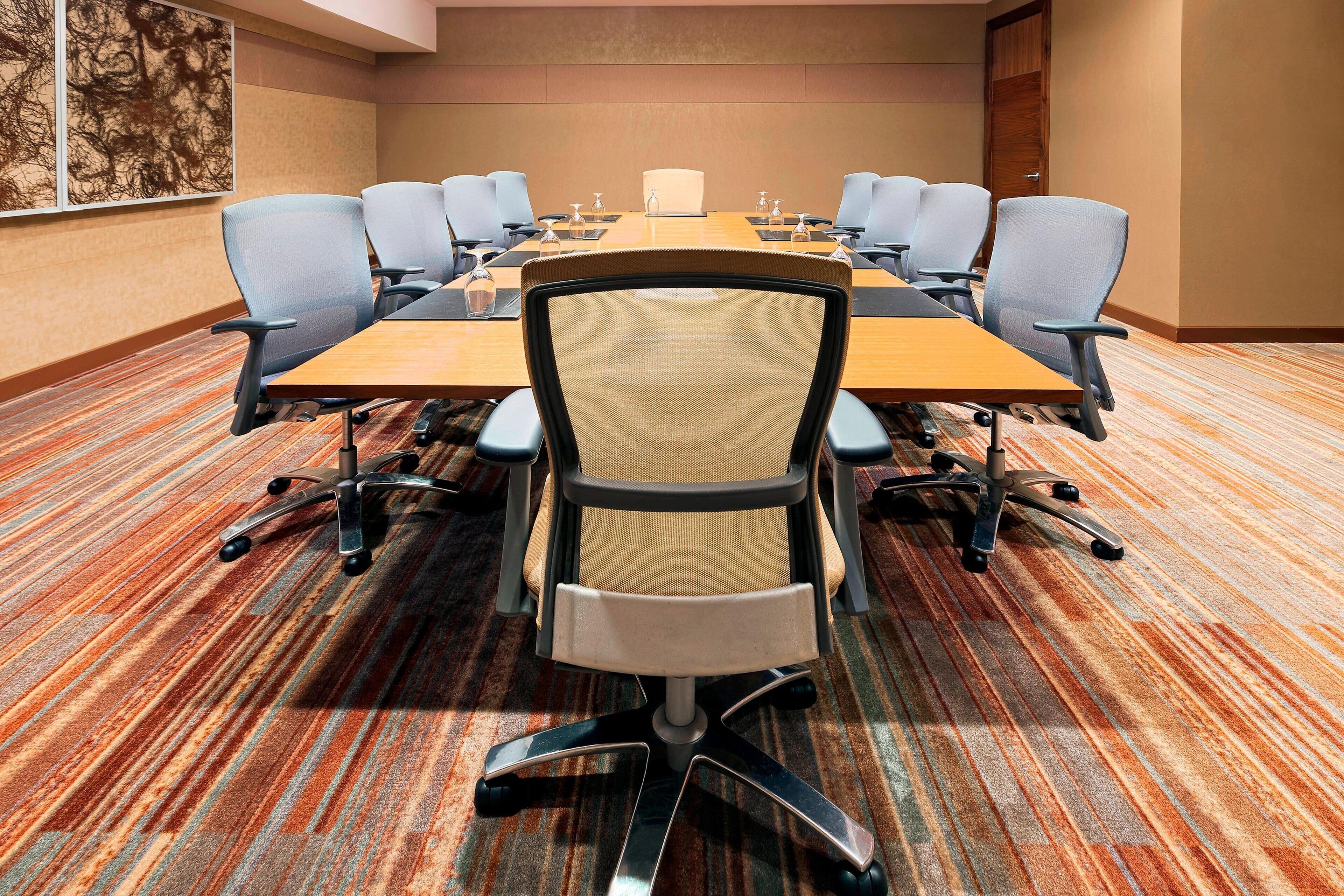 A conference room with a large table, multiple chairs, and a carpeted floor.
