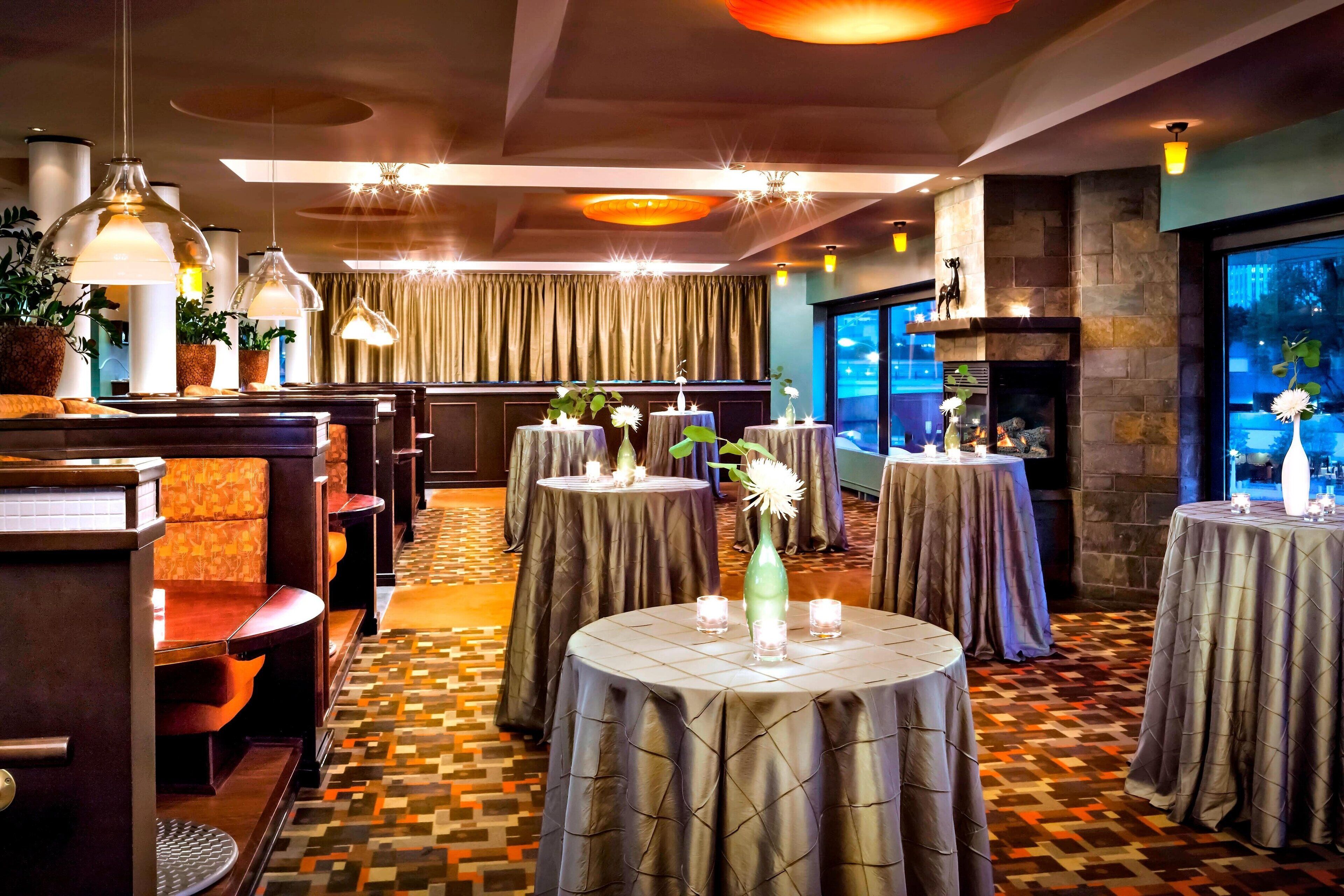 A restaurant with round tables, dark curtains, and hanging pendant lights.
