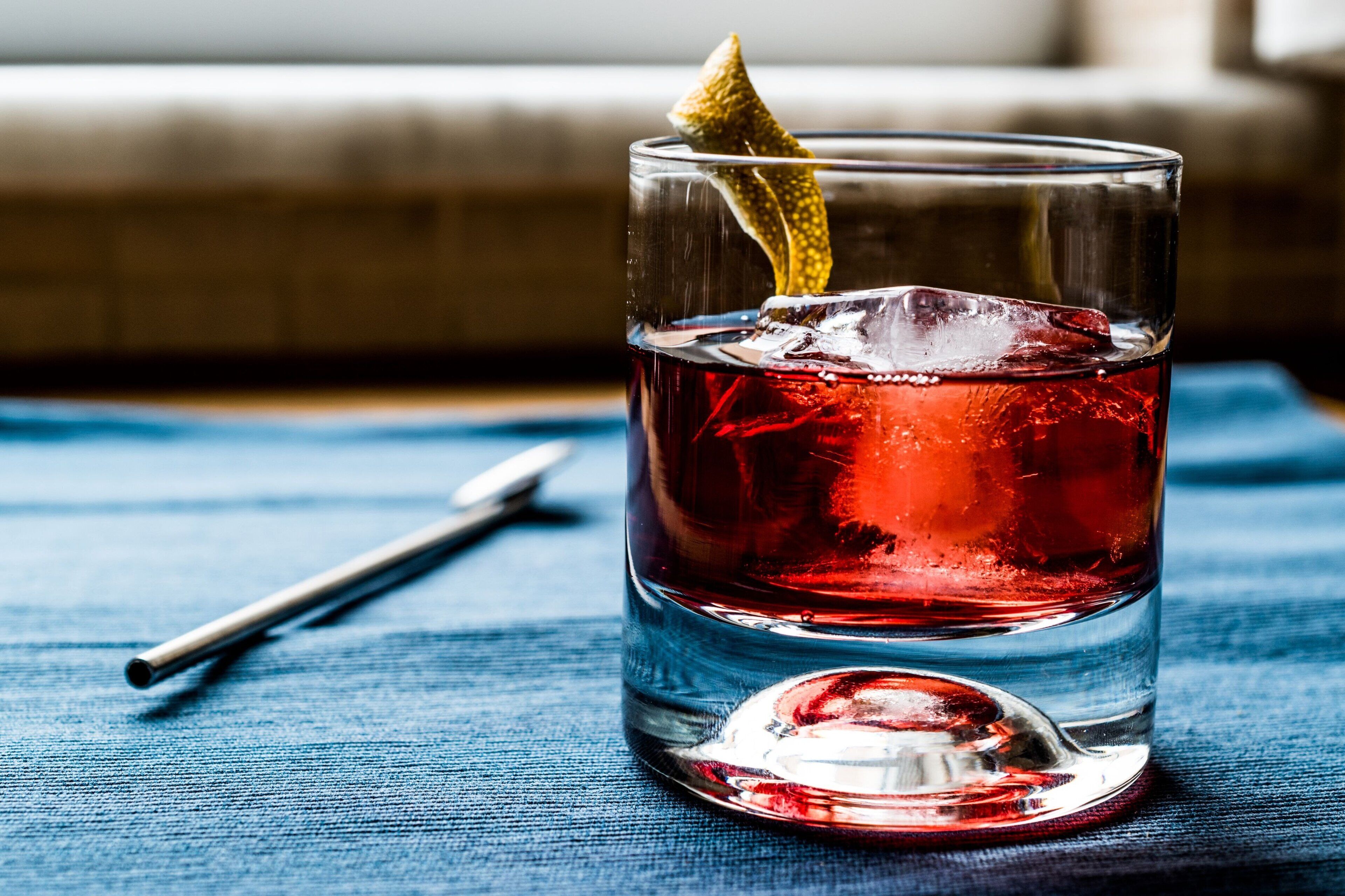 Un vaso transparente con una bebida roja, cubitos de hielo y una rodaja de limón como adorno sobre un paño azul.