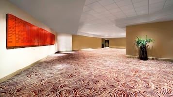 Un pasillo amplio con alfombra estampada, un panel de pared rojo grande y una planta en maceta.