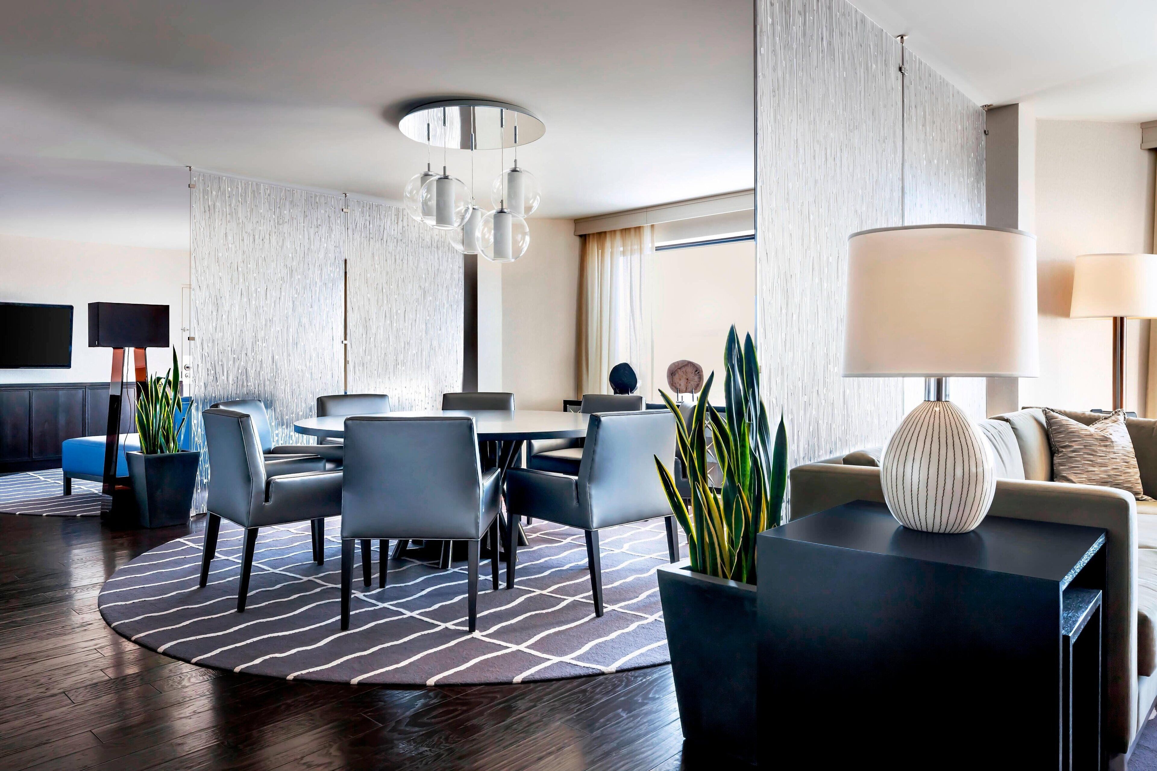 A modern hotel room with a dining area, a sofa, and a large potted plant.