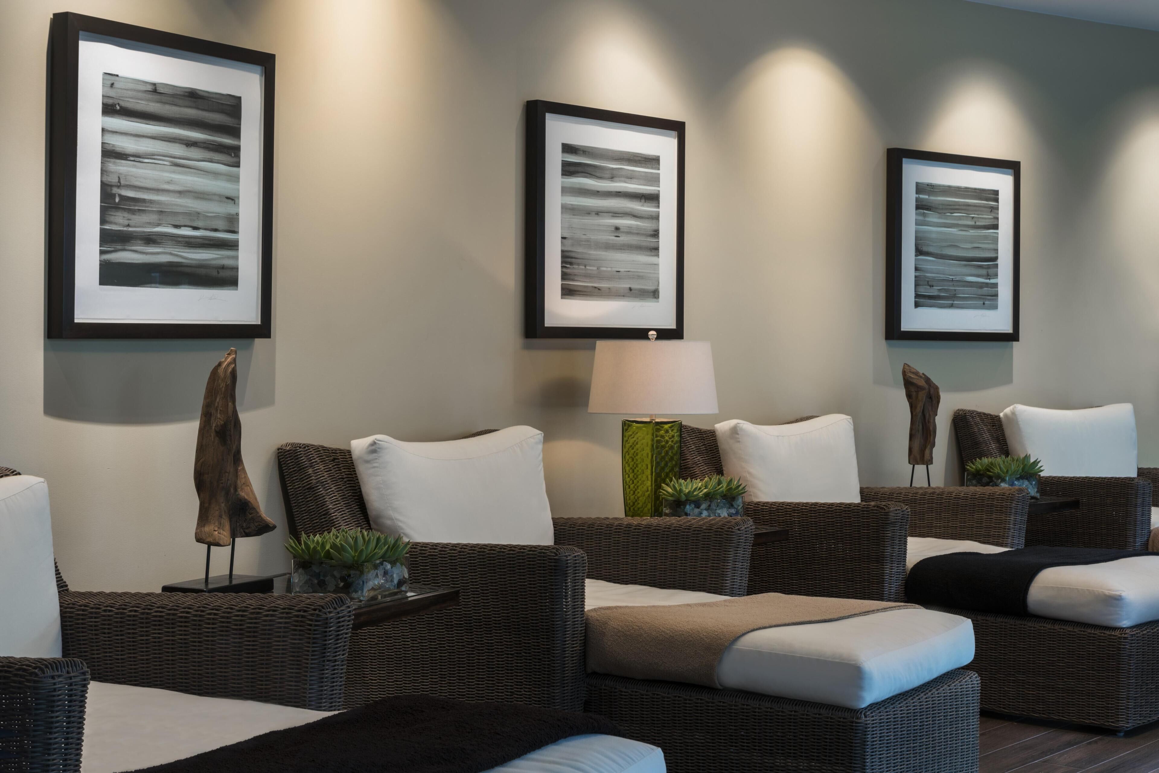A room with wicker furniture, framed artwork on the wall, and a lamp.