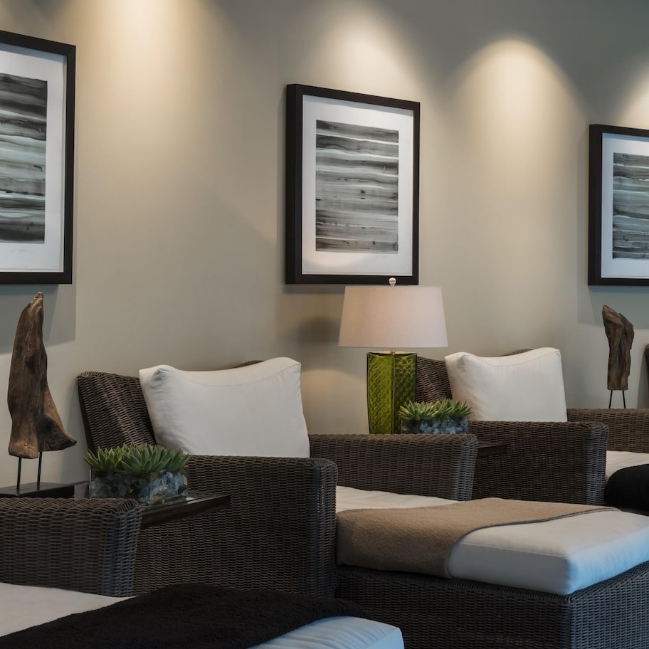 A room with wicker furniture, framed artwork on the wall, and a lamp.