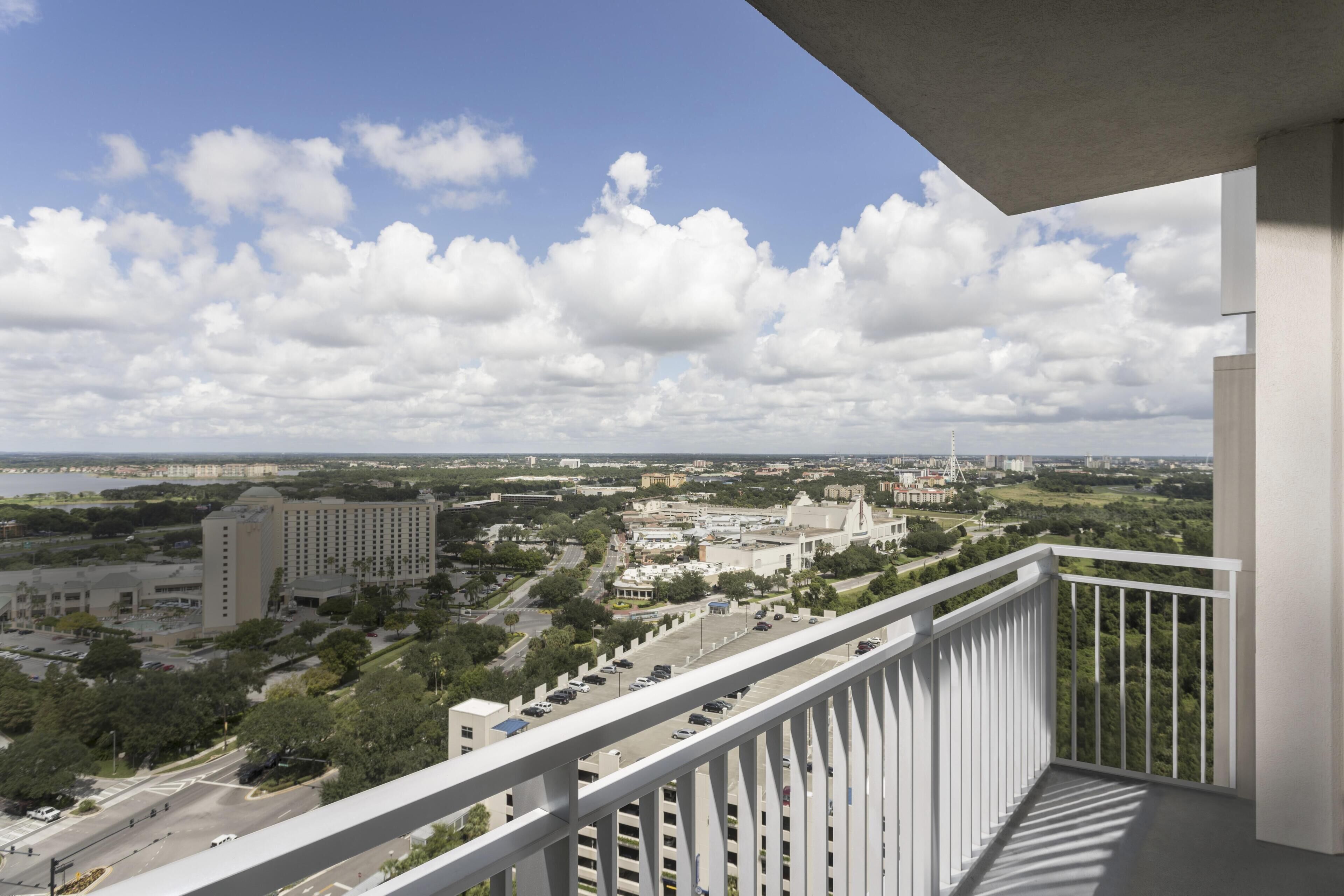 A balcony with a view of a cityscape, including buildings and greenery.