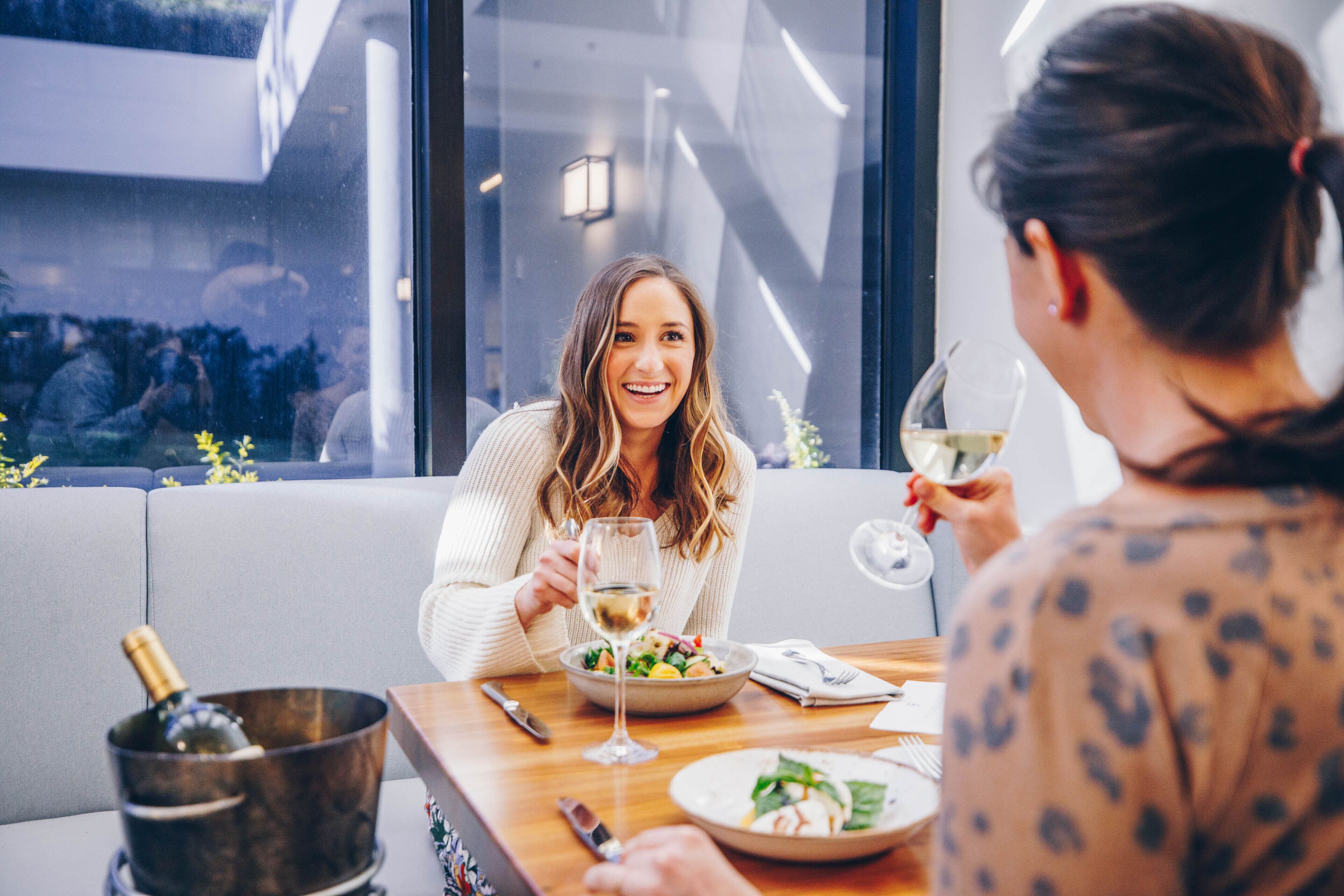 Un coin repas avec une table dressée pour deux personnes, un saladier rempli de salade, une bouteille de vin et un verre à vin.