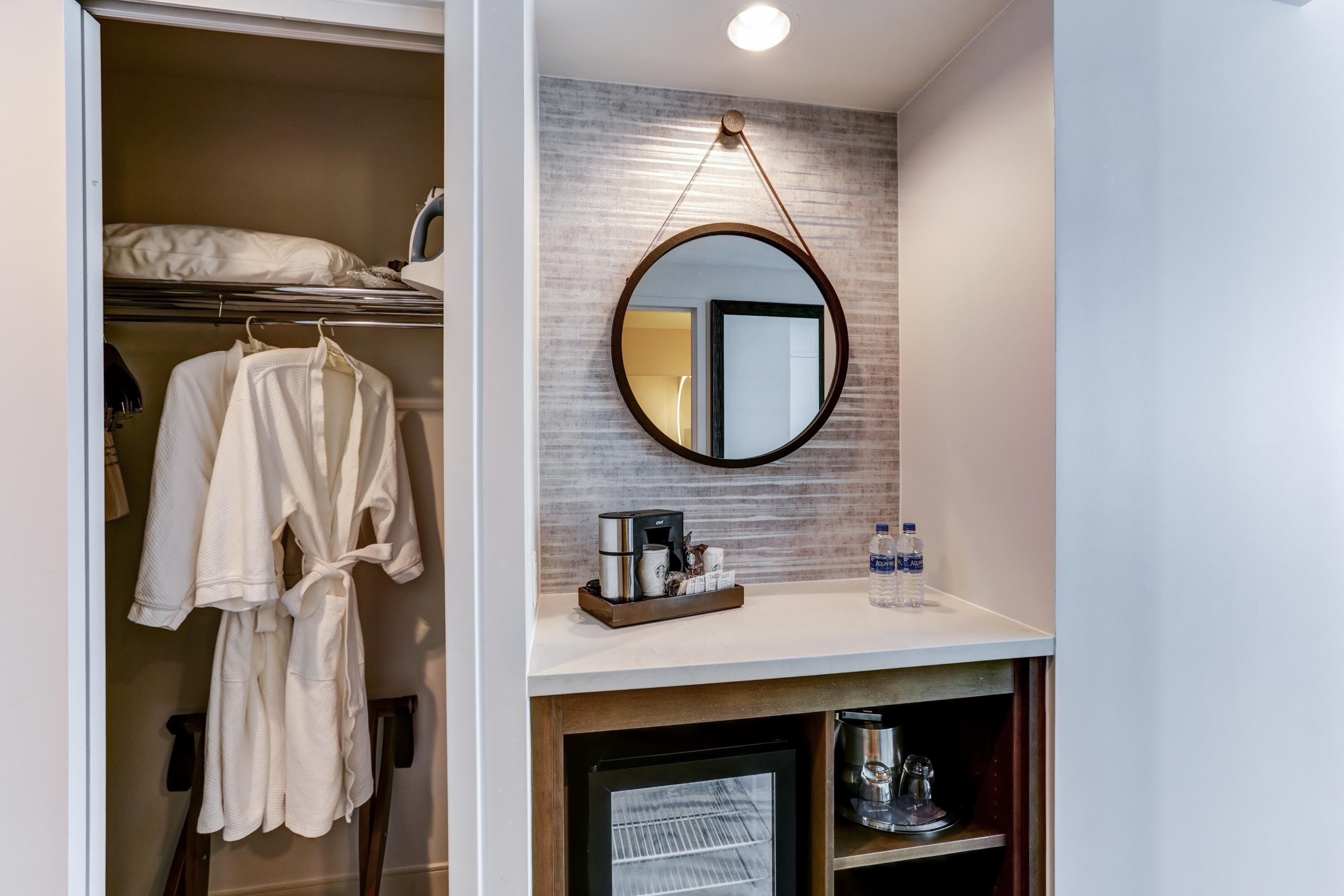 A hotel room with a walk-in closet containing robes, a bed, and a small refrigerator.