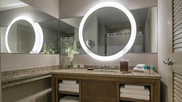 A bathroom with a large mirror, two round lights, a sink, and a towel rack.