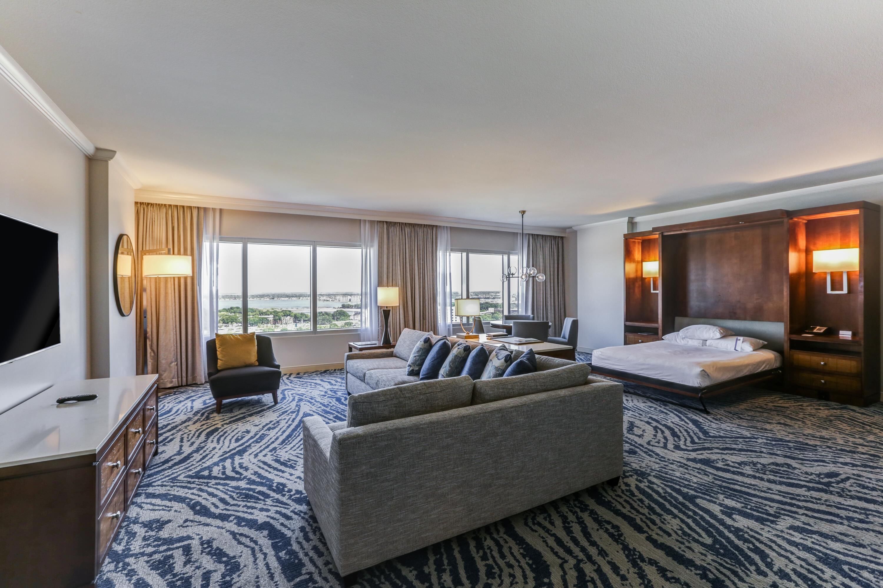 Ein Hotelzimmer mit einem großen Bett, einer Sitzecke, einem Schreibtisch, einem Fernseher und Blick auf die Stadt.