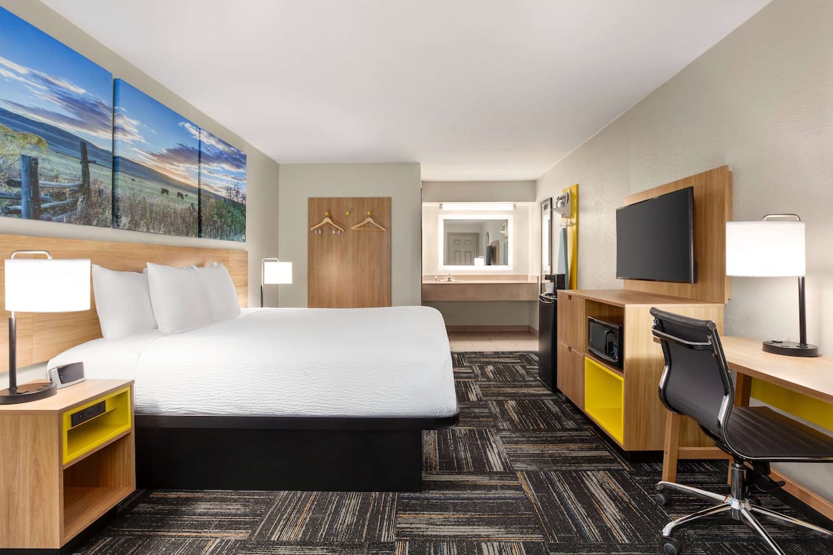 A hotel room with a large bed, a desk with a chair, a TV, and a painting on the wall.