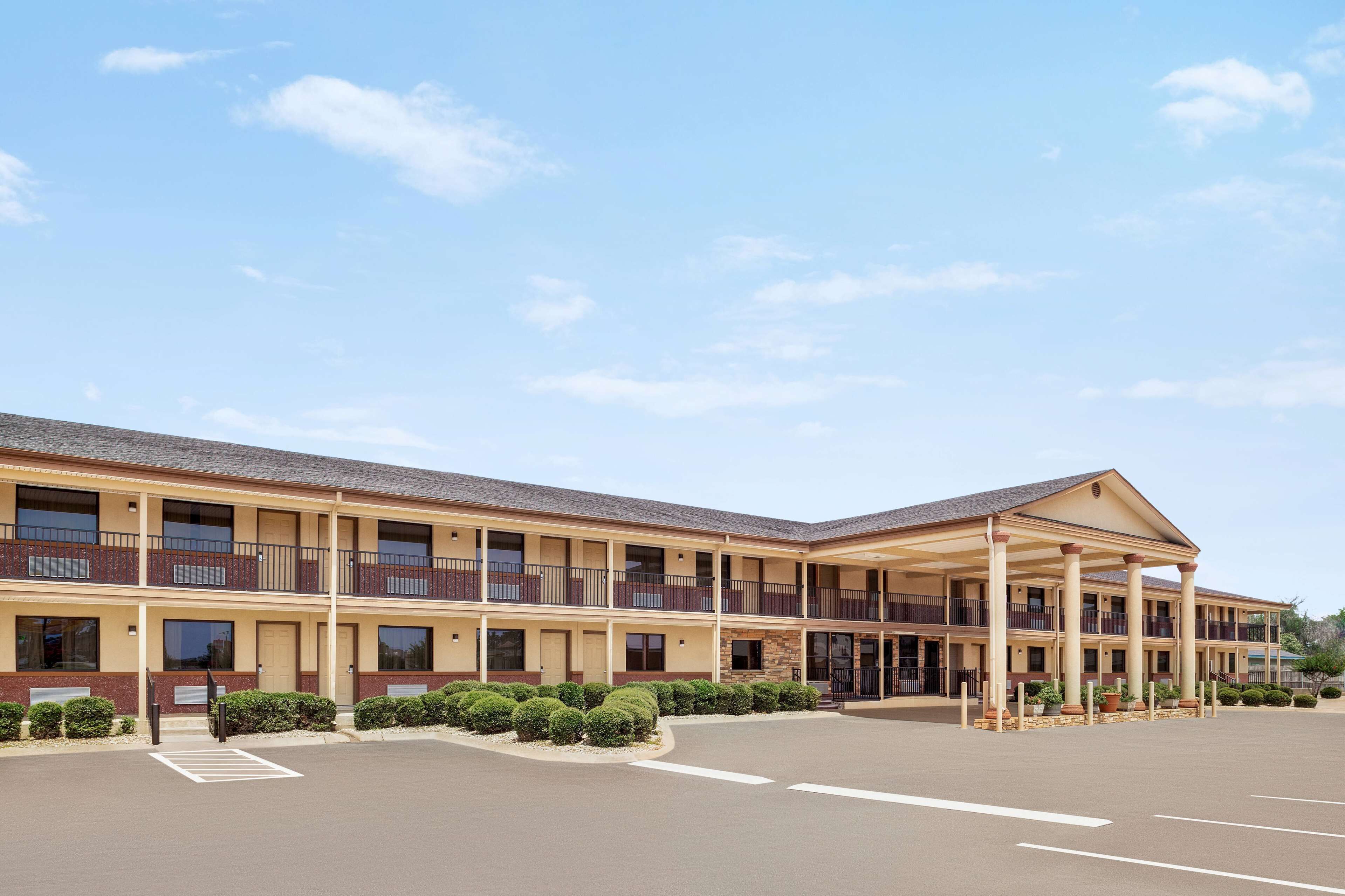 A multi-story motel with a covered front entrance, a parking lot, and a landscaped area with trimmed bushes.