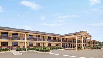 A multi-story motel with a covered front entrance, a parking lot, and a landscaped area with trimmed bushes.