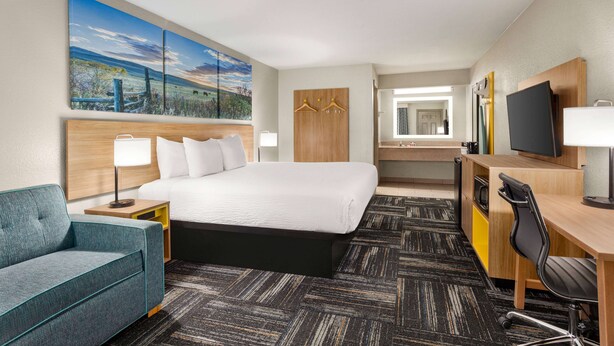 A hotel room with a bed, a desk, a chair, a TV, a wardrobe, and a painting on the wall. - Days Inn by Wyndham Paris (Paris)