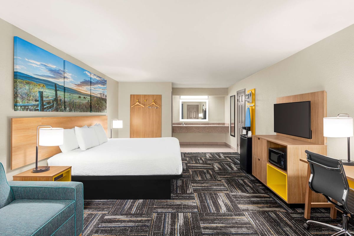 A hotel room with a large bed, a desk with a chair, a TV, and a painting on the wall.