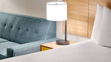 Ein modernes Hotelzimmer mit einem blau gepolsterten Sofa, einem Nachttisch mit Lampe und einem hölzernen Kopfteil.
