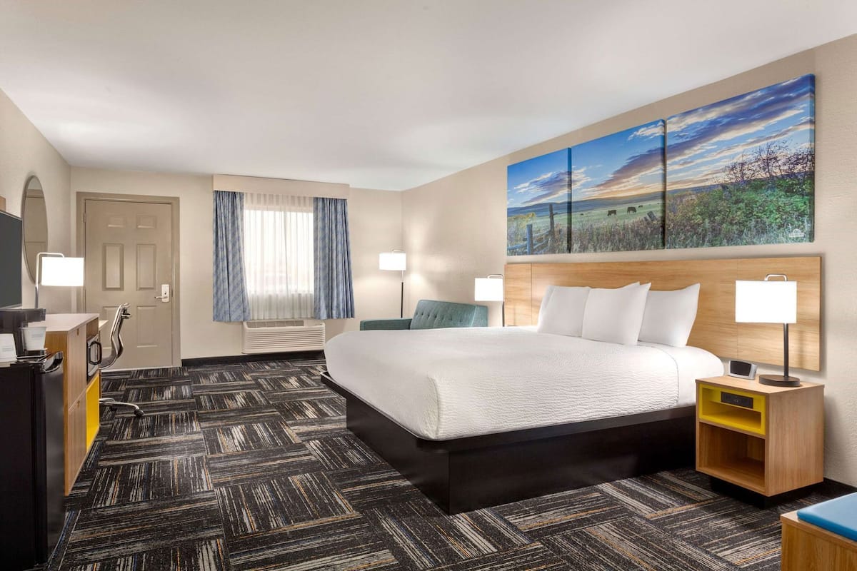 A hotel room with a large bed, a desk with a computer, a TV, and a painting on the wall.