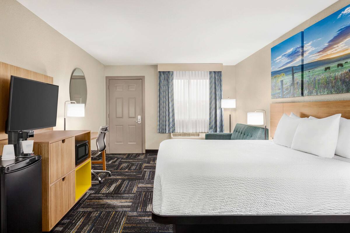 A hotel room with a large bed, a desk with a flat-screen TV, a microwave, and a seating area with a chair and a table.