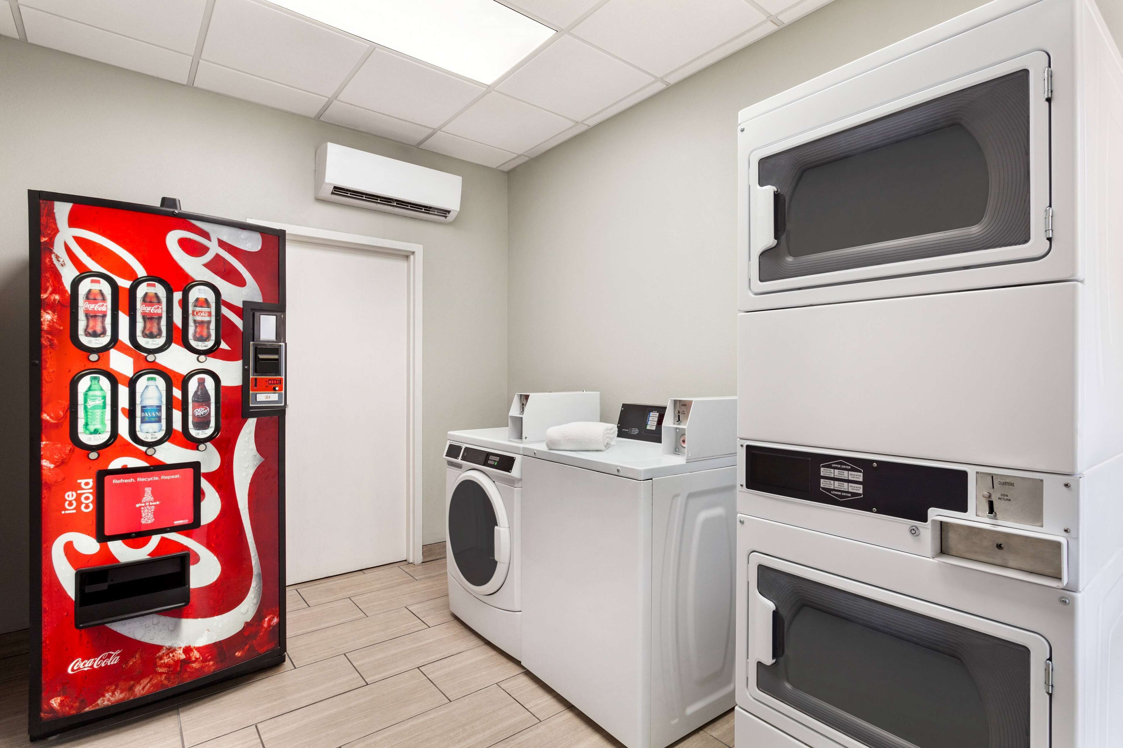 Une buanderie équipée d’un distributeur automatique de Coca-Cola, d’une machine à laver et de plusieurs sèche-linge superposés.