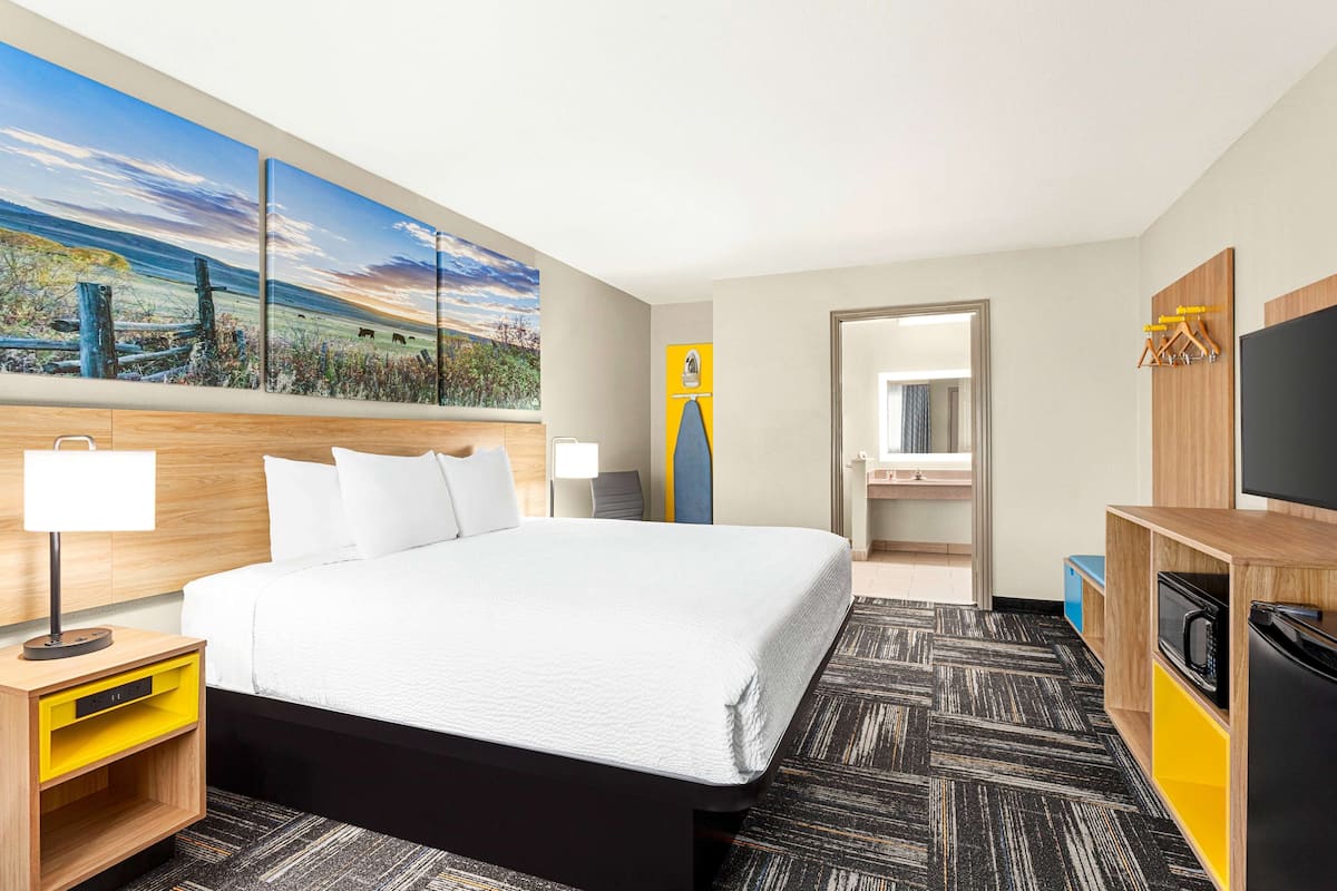 A hotel room with a large bed, a flat-screen TV, a microwave, and a bathroom visible through an open door.