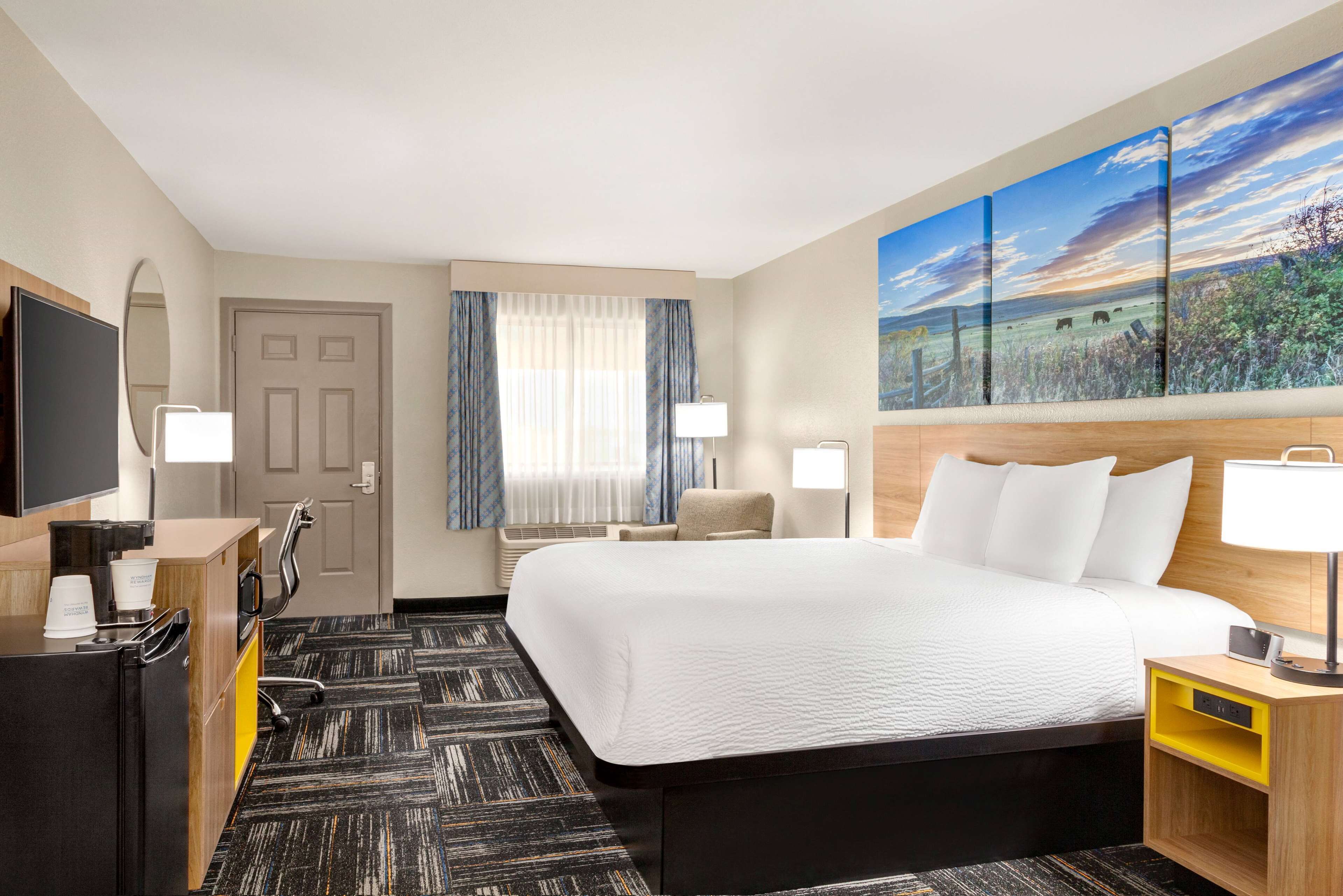 Una habitación de hotel con una cama grande, un escritorio con ordenador, televisión y un cuadro en la pared.