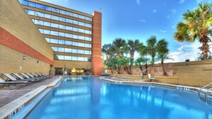 A swimming pool with lounge chairs, a brick building, and palm trees.