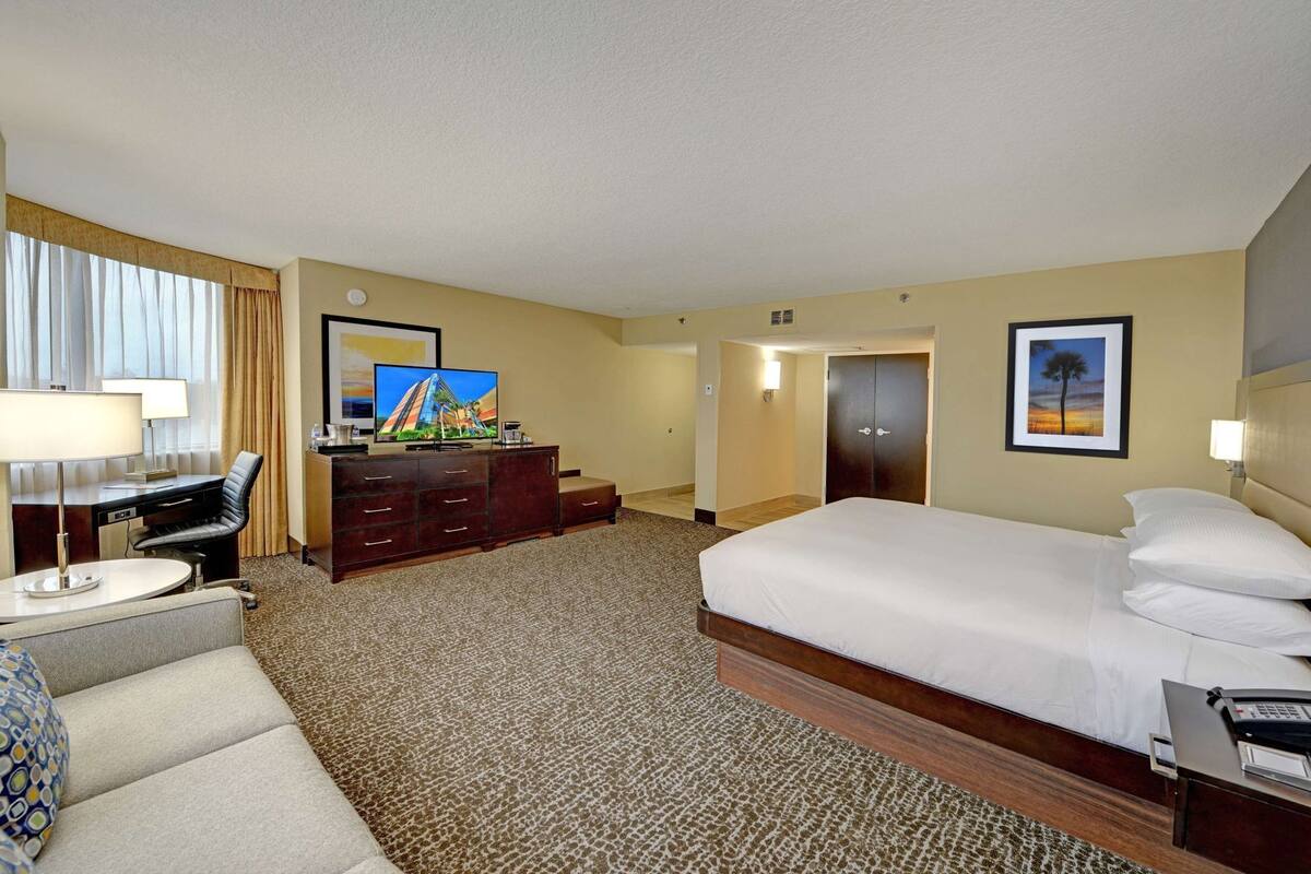 A hotel room with a bed, desk, chair, television, and a framed picture on the wall.