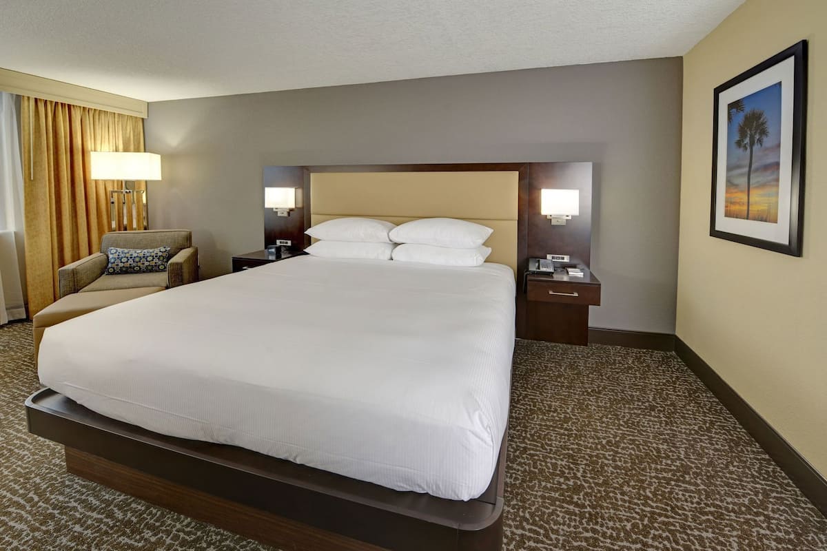 A hotel room with a large bed, two bedside tables, a chair, a lamp, and a framed picture on the wall.