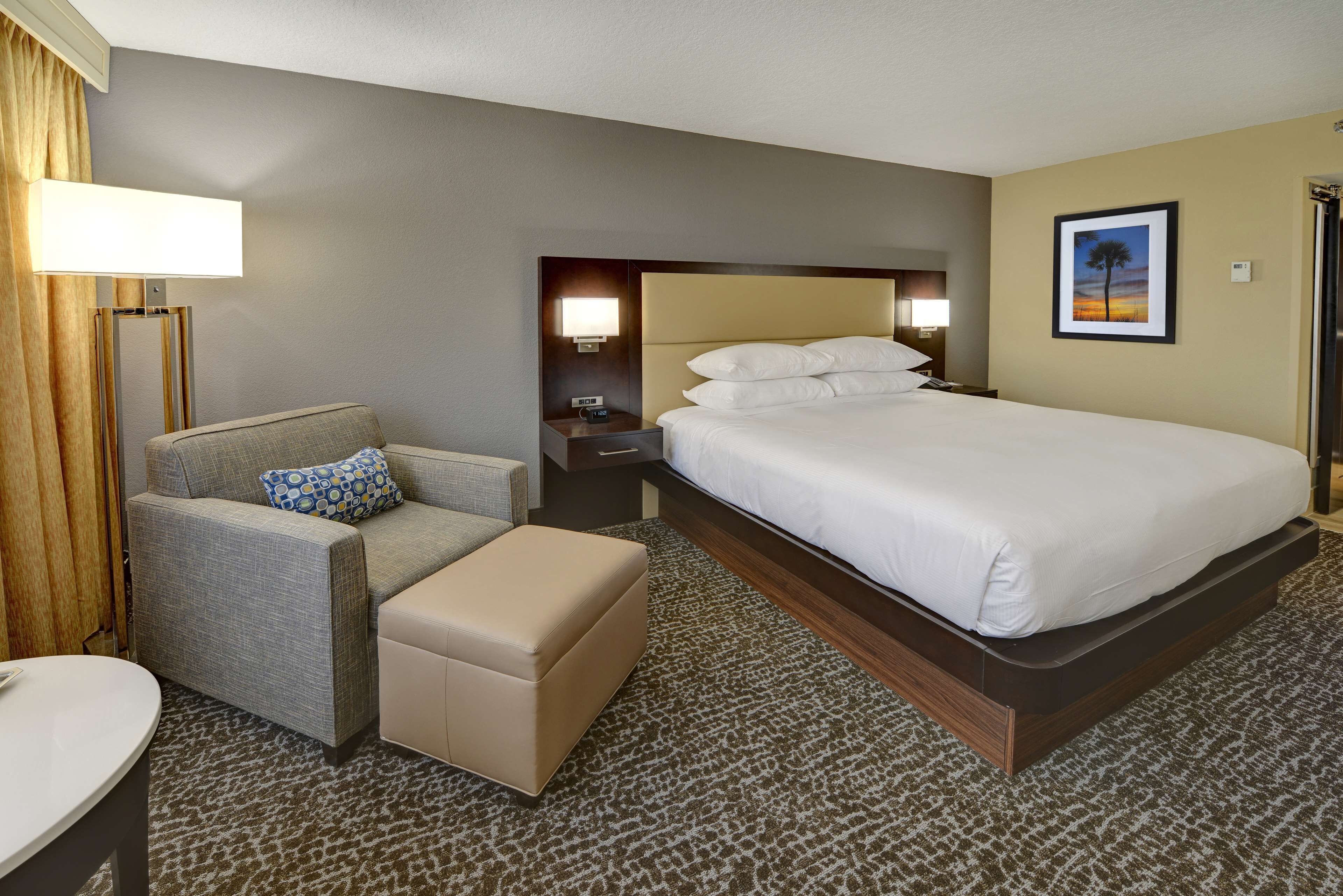 A hotel room with a large bed, a sofa, a small table, and a nightstand with a lamp.