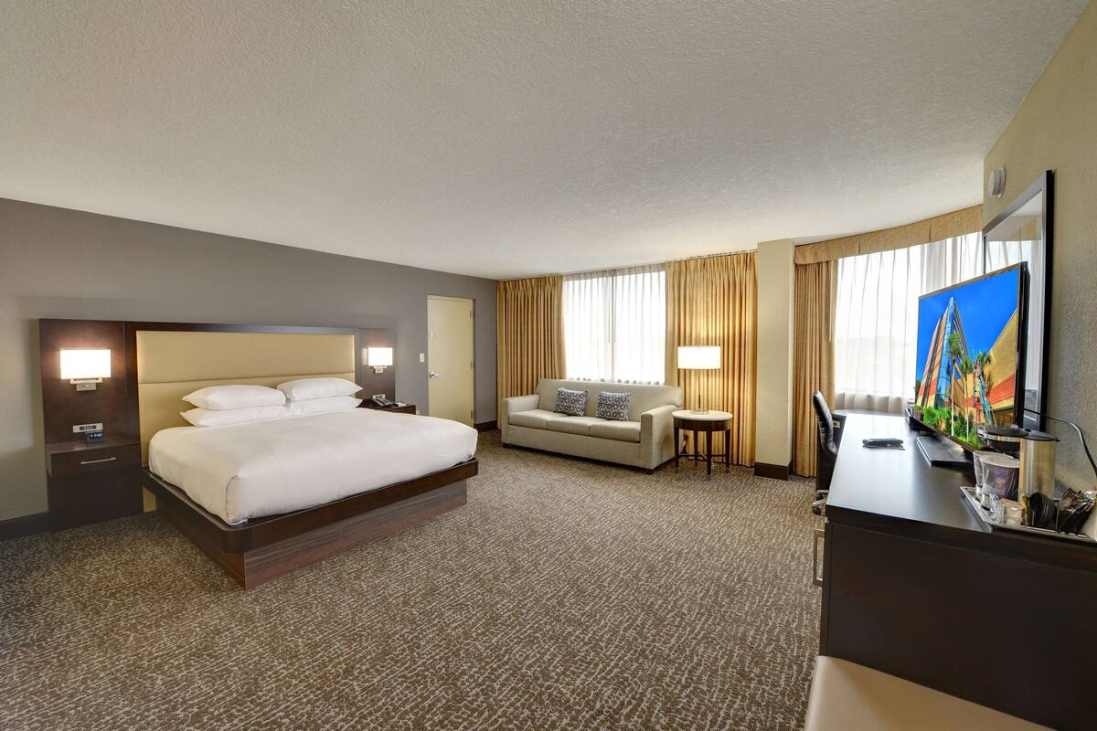 A hotel room with a large bed, a sofa, a desk, and a television.