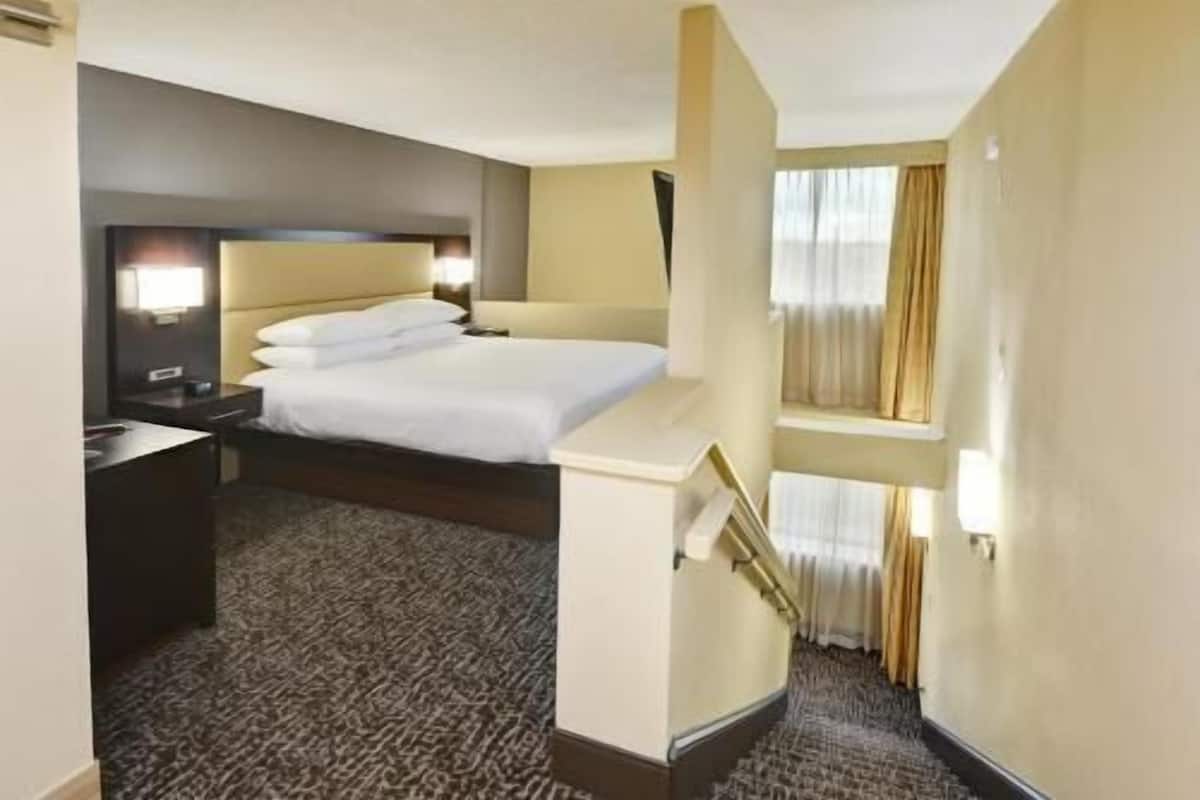 A hotel room with a bed, a desk, a nightstand, and a window with curtains.