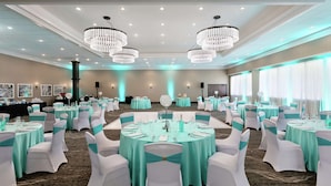 A banquet hall with round tables, white chairs, teal tablecloths, and chandeliers.