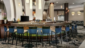 A bar area with a curved counter, multiple bar stools, and hanging pendant lights.