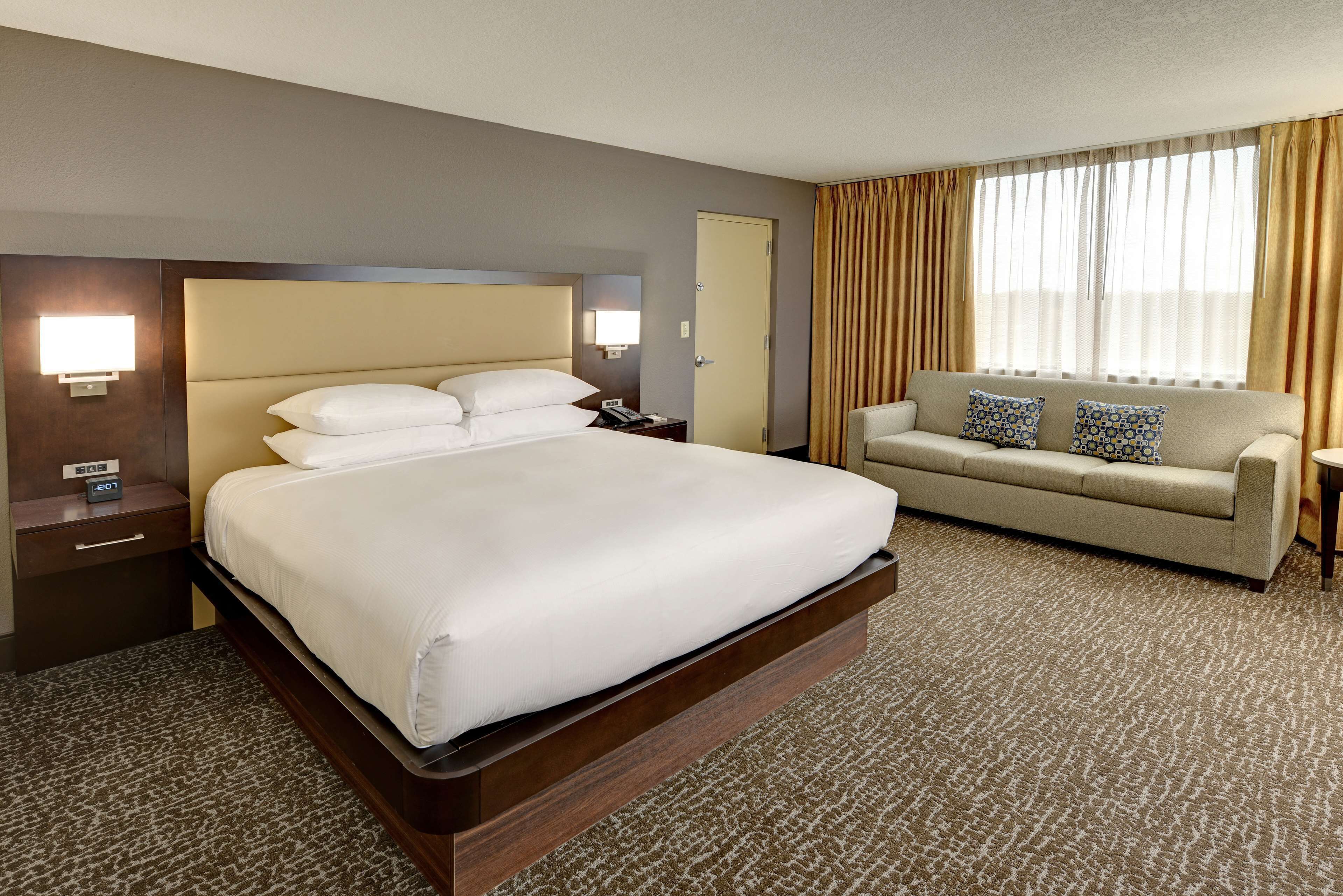A hotel room with a large bed, a sofa, a nightstand, and a lamp.
