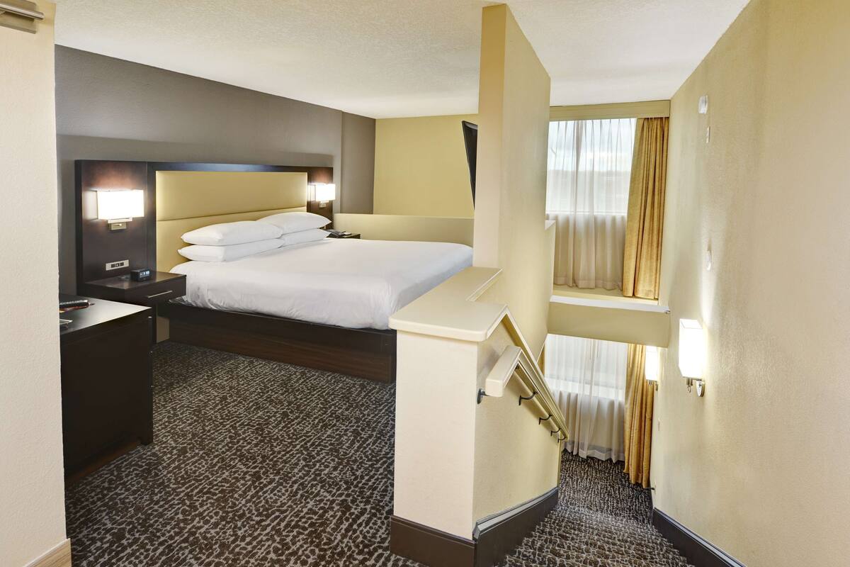 A hotel room with a large bed, a desk, a nightstand, and a window with curtains.