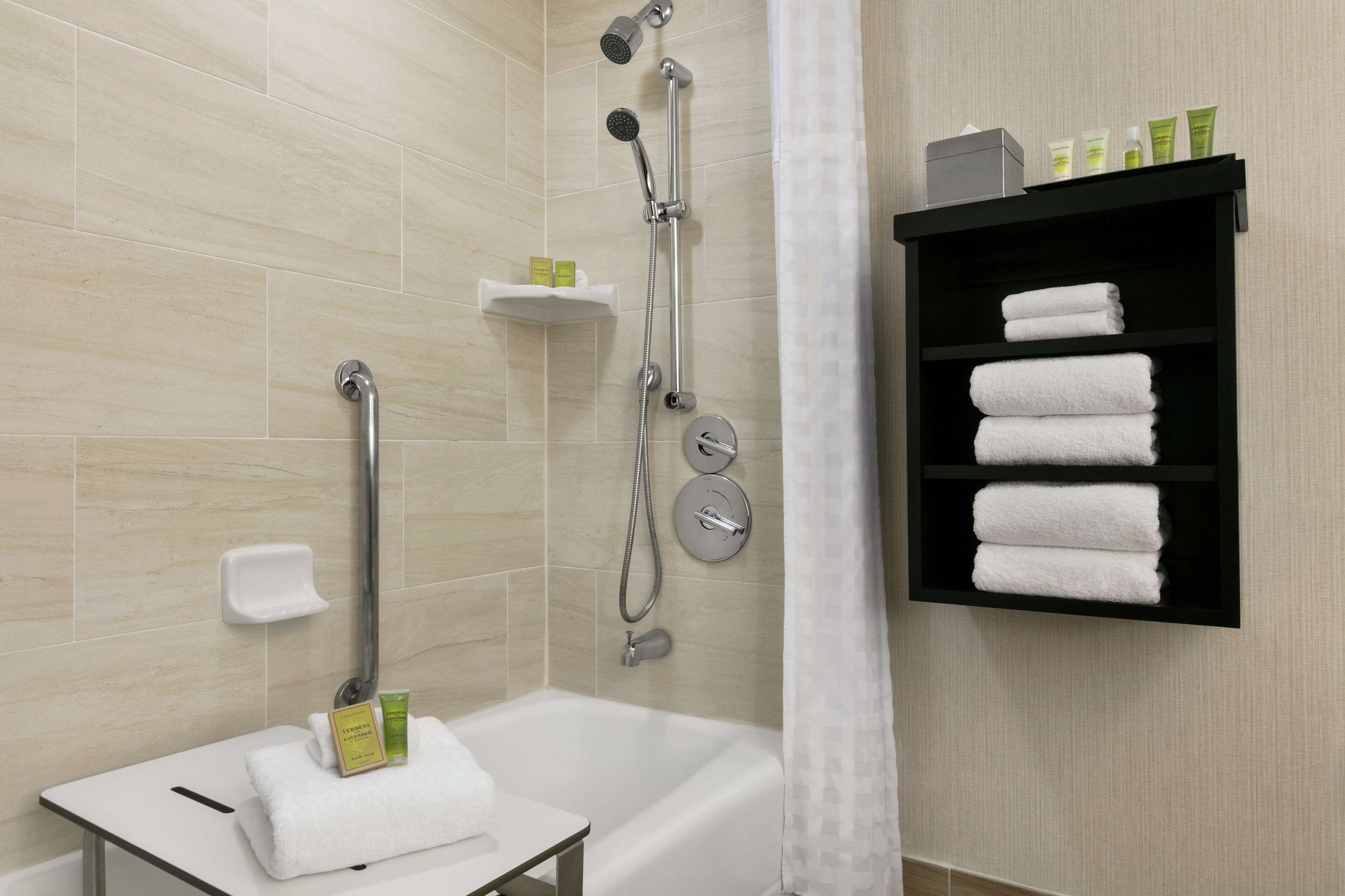 A modern bathroom with a bathtub, a shower with a handheld showerhead, a towel rack with folded towels, and a shelf with toiletries.