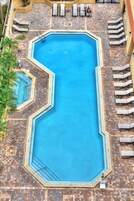 Una piscina octagonal con solárium de baldosas, rodeada de sillas de descanso y una palmera.