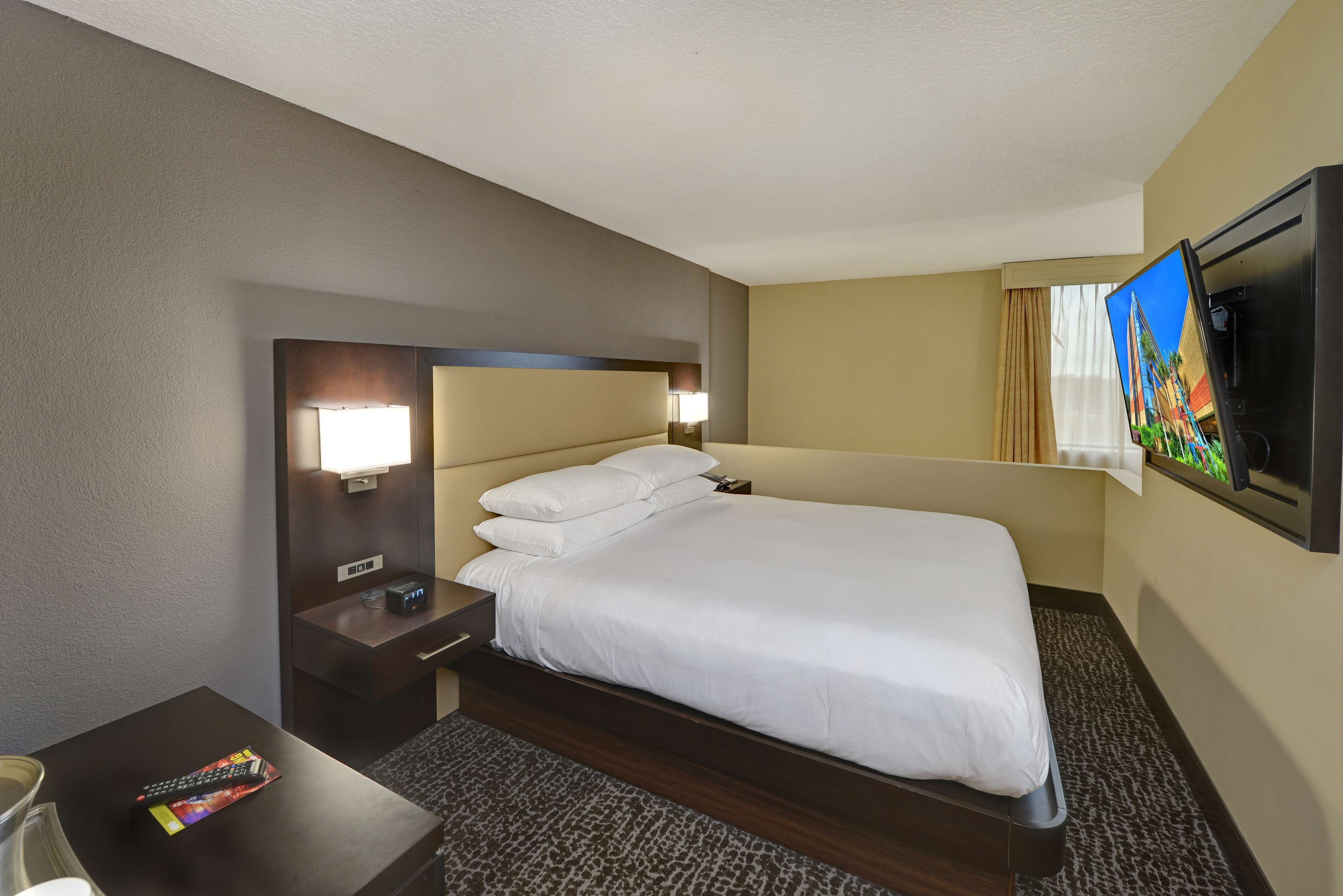 A hotel room with a bed, a desk, a TV, and a window with curtains.