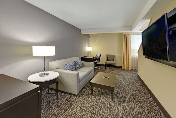 A hotel room with a sofa, a small round table, a coffee table, a TV, and a carpeted floor.
