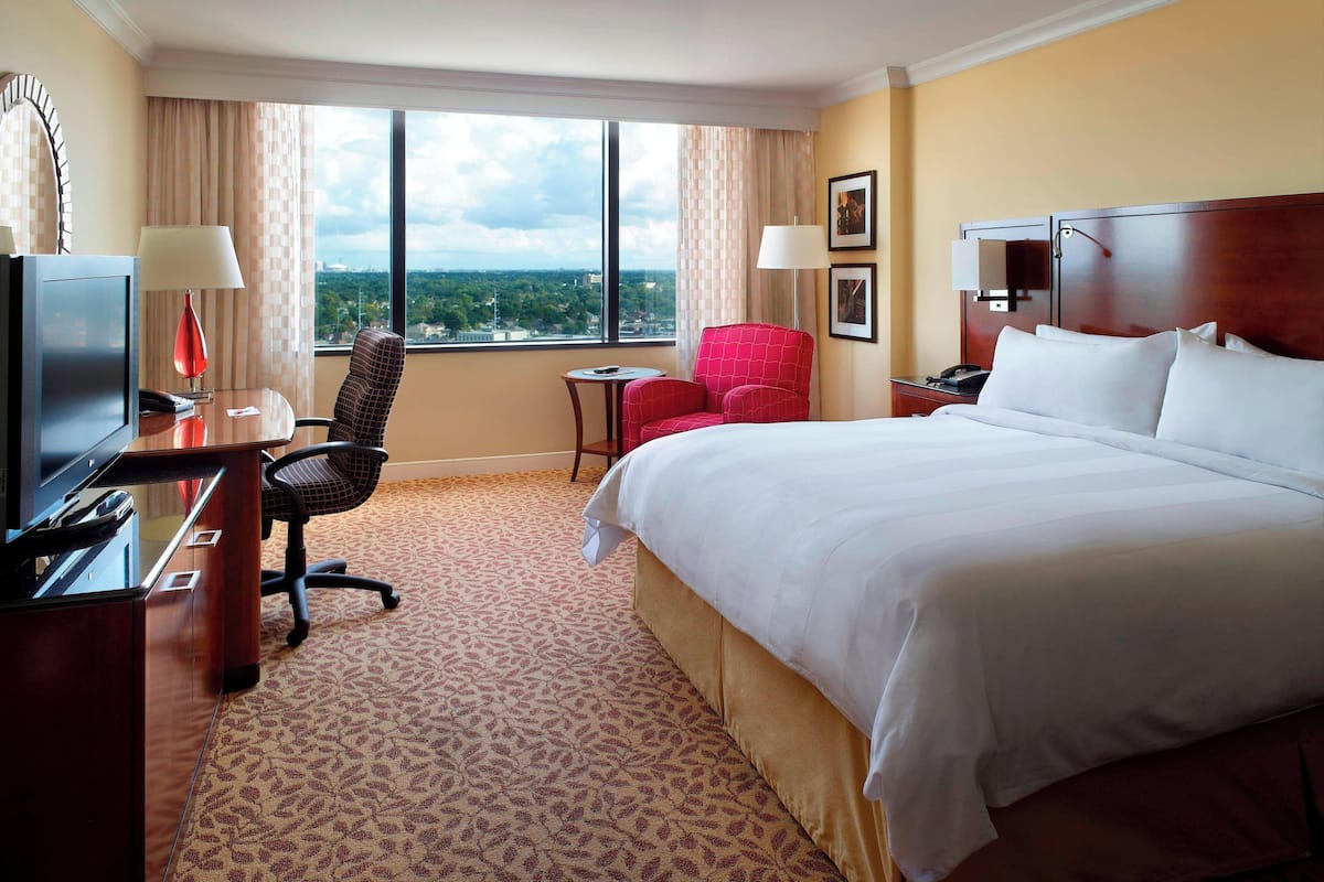Habitación de hotel con una cama grande, un escritorio con computadora, una silla, una mesita y una ventana con vista a la ciudad.