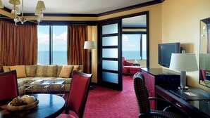 Habitación de hotel con sofá, sillas, una mesa de comedor, televisor y vista al mar.