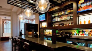 Zona de bar con techo alto, lámparas esféricas colgantes y una pantalla de televisión mostrando un programa.