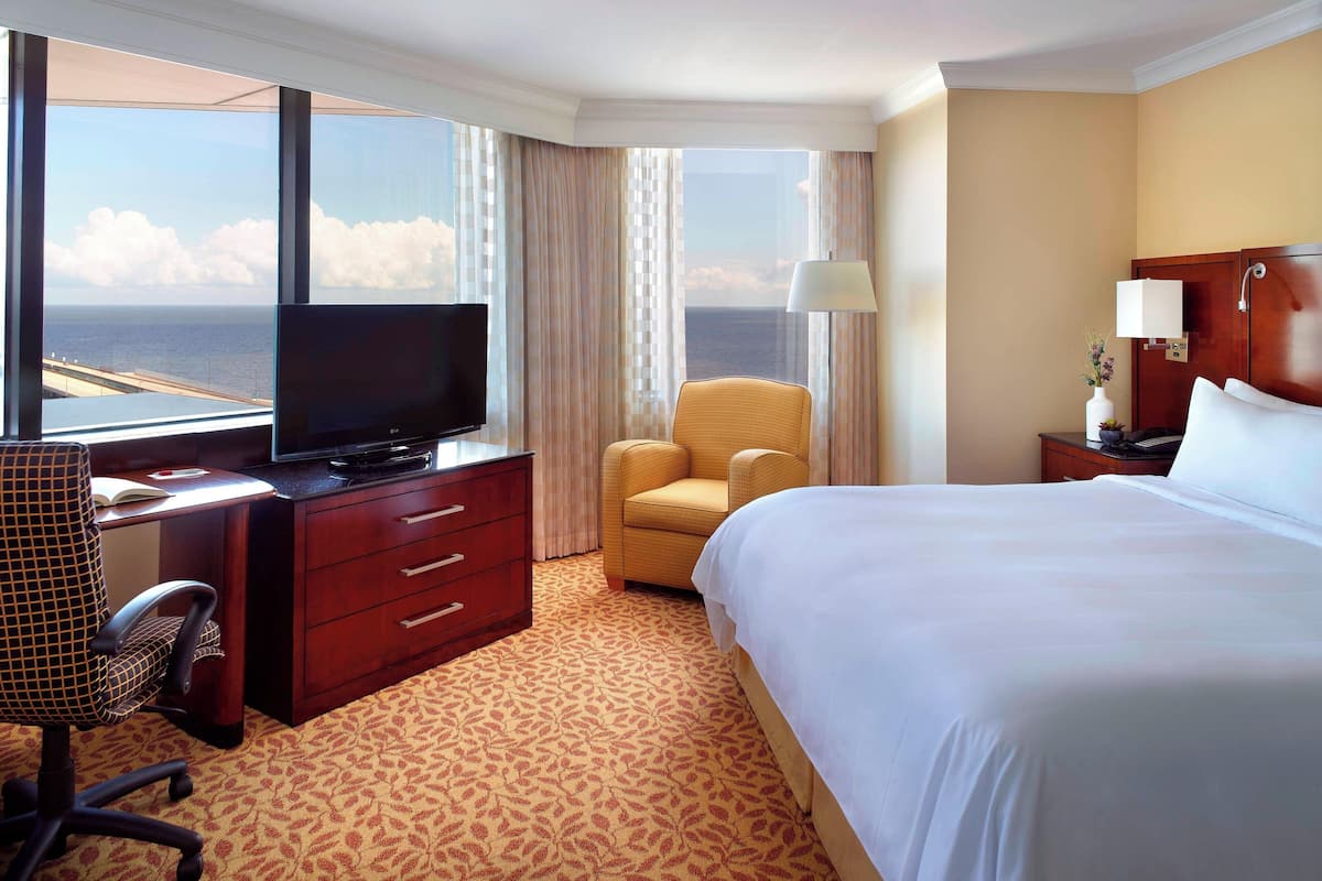 Habitación de hotel con cama, escritorio con televisor, silla y vista al océano.