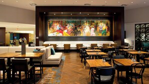 Un restaurante moderno con un gran mural, mesas de madera y una variedad de opciones de asiento, incluyendo sofás y sillas.