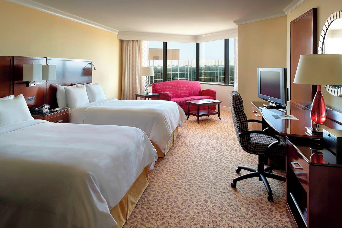 Habitación de hotel con dos camas, un escritorio con computadora, televisor y una silla roja.