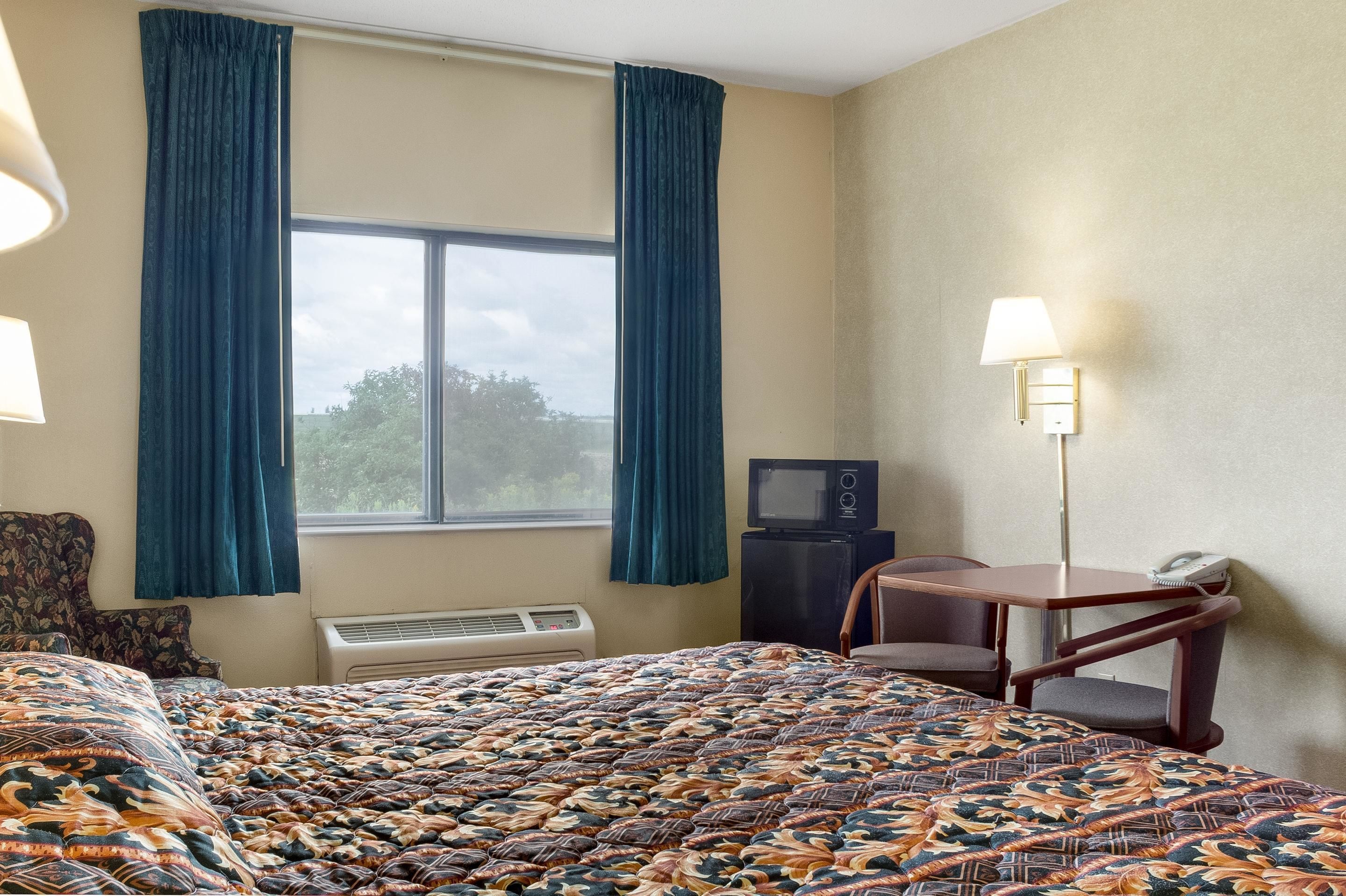 Een hotelkamer met een bed, een bureau, een stoel, een televisie en een raam met gordijnen.