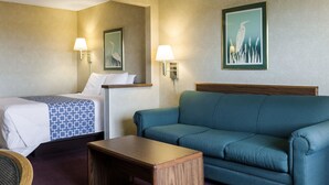 Una camera d'albergo con un letto, un divano, un piccolo tavolino in legno e due lampade a parete.