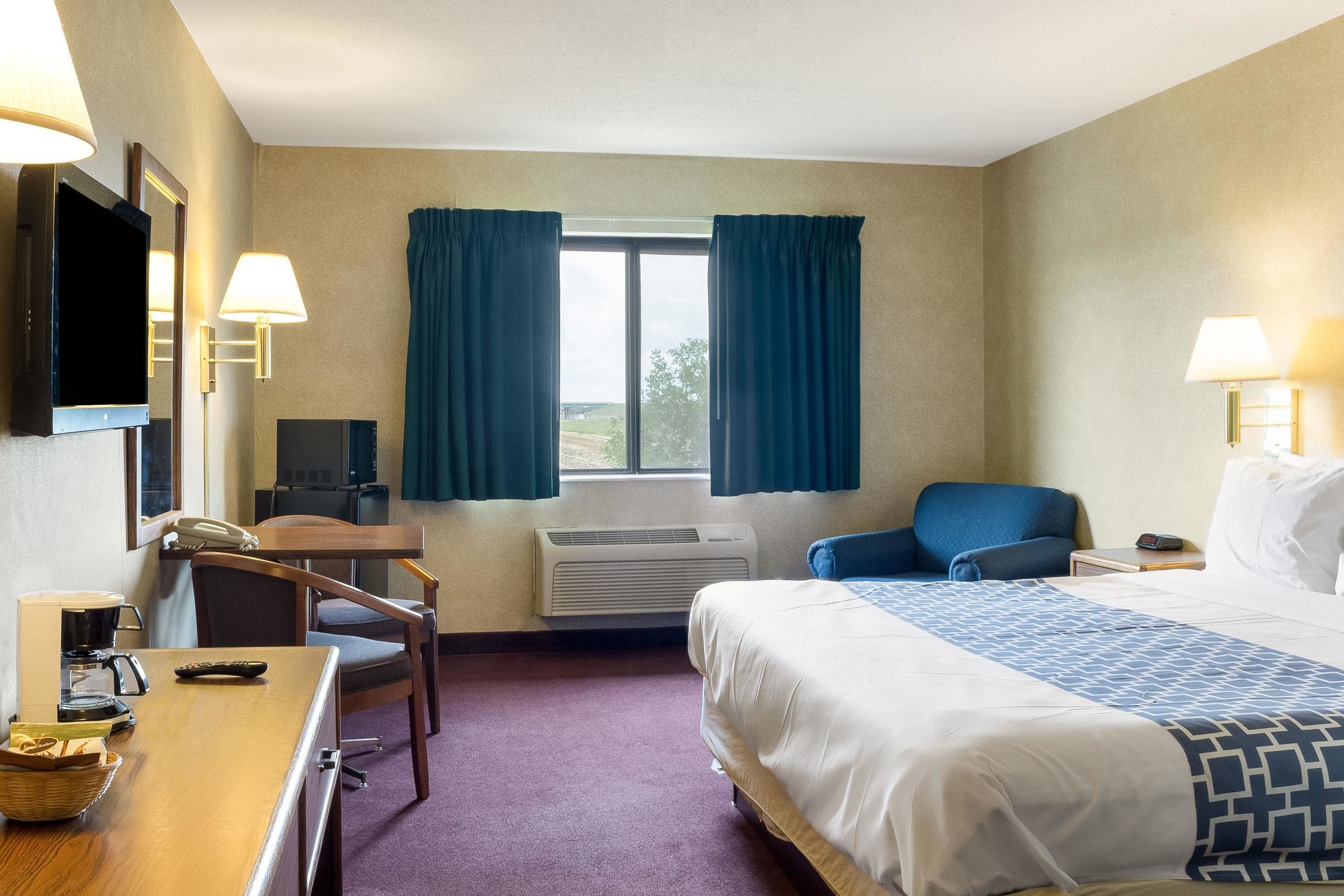 Una habitación de hotel con cama, escritorio con silla, televisor y aire acondicionado.