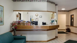 Una zona reception con una scrivania in legno, un orologio, quadri incorniciati e un divano verde.