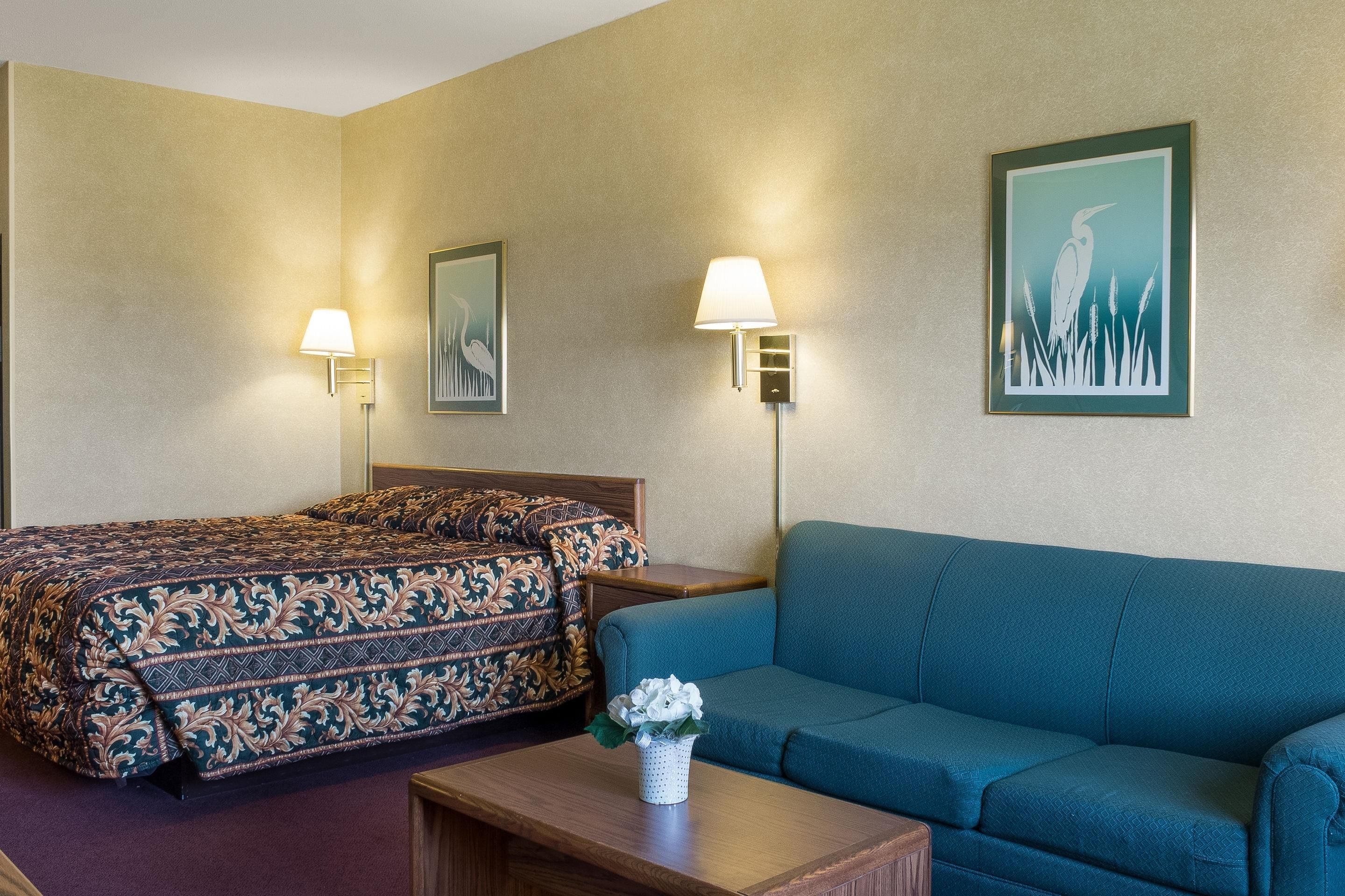 A hotel room with a bed, a blue sofa, a small table with a vase, and two wall-mounted lamps.