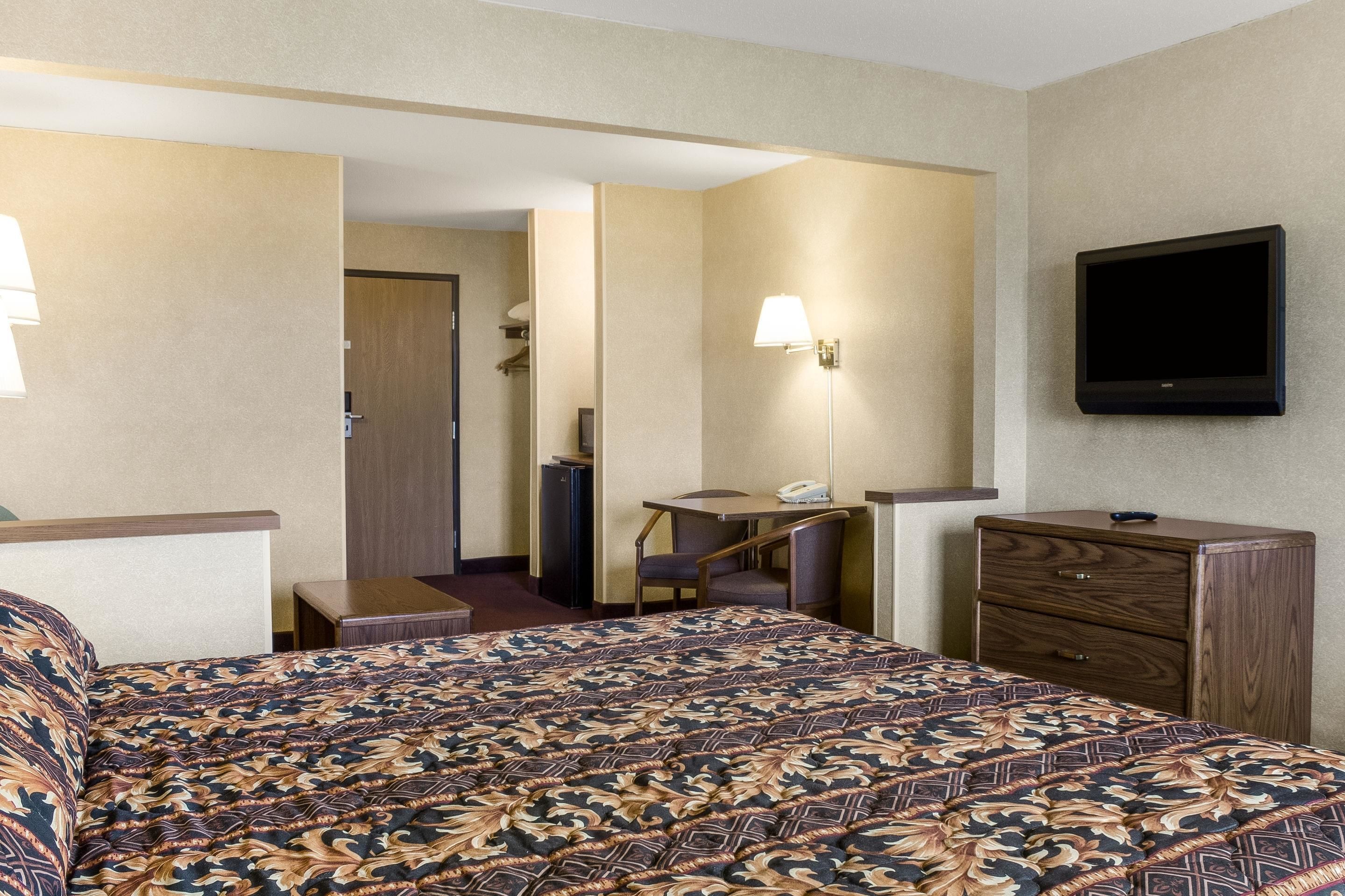 A hotel room with a large bed, a desk, a chair, a dresser, and a TV mounted on the wall.