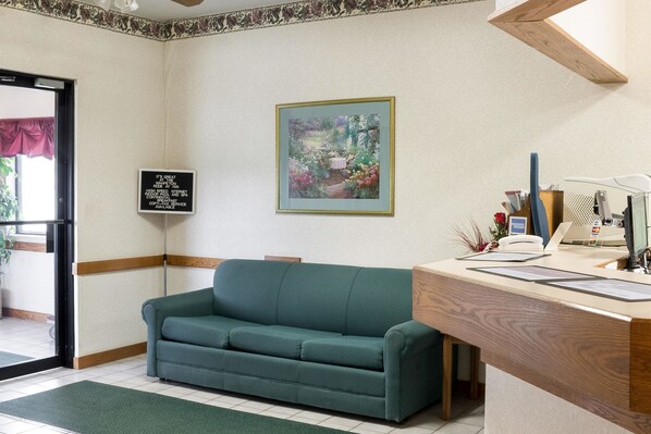 A reception area with a green sofa, a wooden desk, a framed painting, and a signboard.